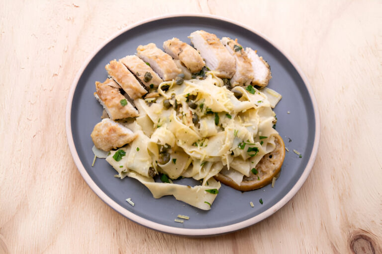 A plate of sliced chicken breast served with creamy pasta and garnished with herbs.