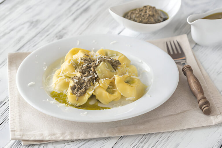 A plate of tortellini pasta topped with herbs and grated cheese, served on a beige cloth