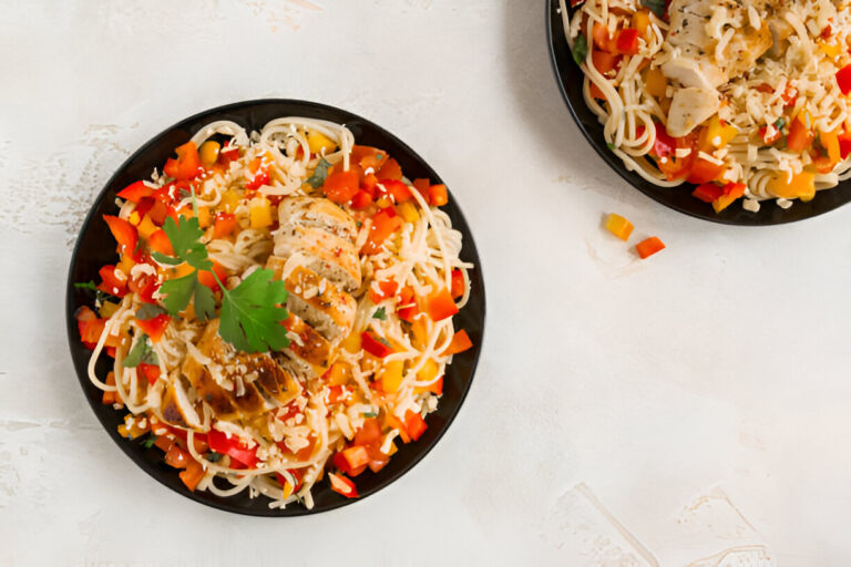 A vibrant plate of spaghetti topped with grilled chicken, colorful bell peppers, and garnished with fresh herbs.