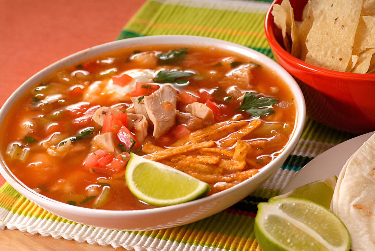 A delicious bowl of chicken tortilla soup topped with chopped tomatoes and cilantro, served with lime slices and tortilla chips.