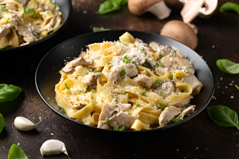 A delicious plate of fettuccine pasta topped with creamy sauce, sliced mushrooms, and fresh parsley, served in a black bowl.