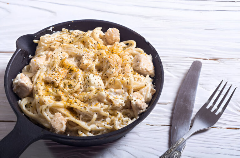 Creamy chicken fettuccine in a black cast iron skillet with fork and knife on a wooden table.