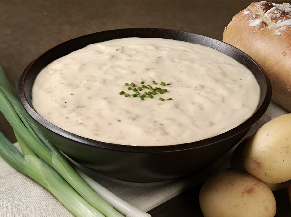 A bowl of creamy soup garnished with chopped chives, served with green onions and potatoes on the side.