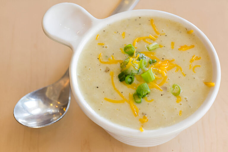 A bowl of creamy soup topped with shredded cheese and chopped green onions.