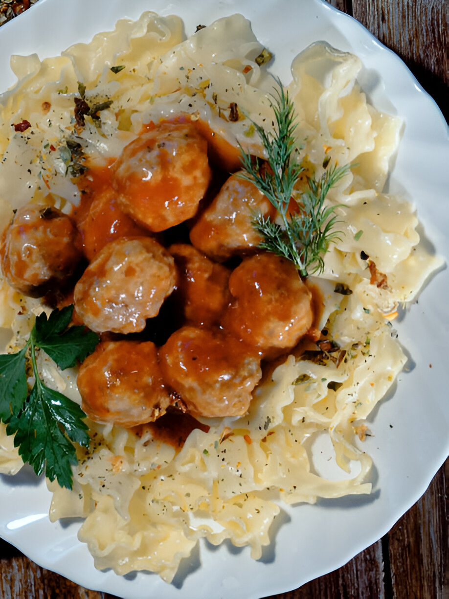 A plate of noodles topped with meatballs and sauce, garnished with fresh herbs.