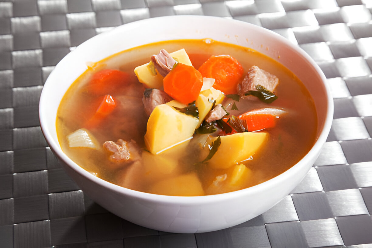 A hearty bowl of vegetable and meat soup featuring chunks of potatoes, carrots, and herbs in a savory broth.