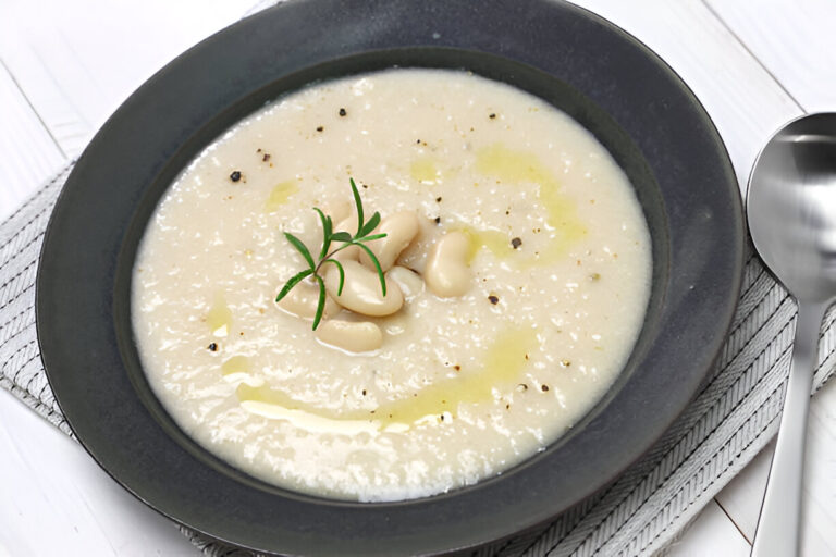 A bowl of creamy white bean soup garnished with herbs and drizzled with olive oil