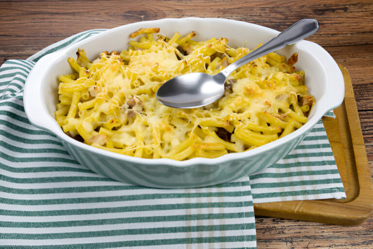 A ceramic dish filled with cheesy pasta, topped with melted cheese and a spoon resting on the side.