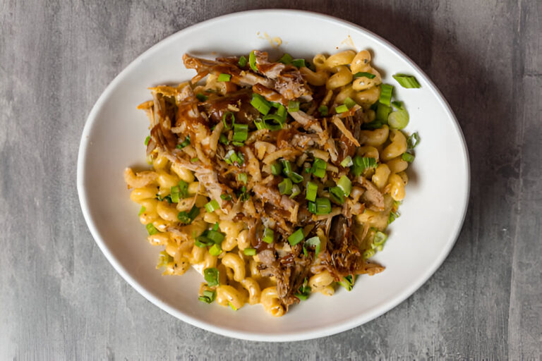 A plate of creamy macaroni pasta topped with shredded meat and green onions