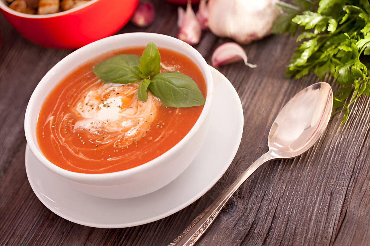 A bowl of tomato soup garnished with basil leaves on a wooden table.