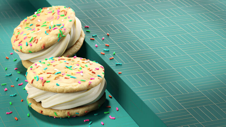 Two large cookie sandwiches filled with creamy frosting and topped with colorful sprinkles, placed on a teal surface.