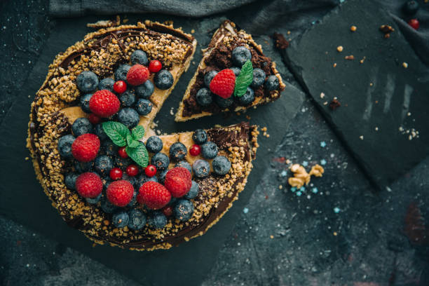 A decadent chocolate cake topped with fresh raspberries, blueberries, and mint leaves on a dark slate surface.