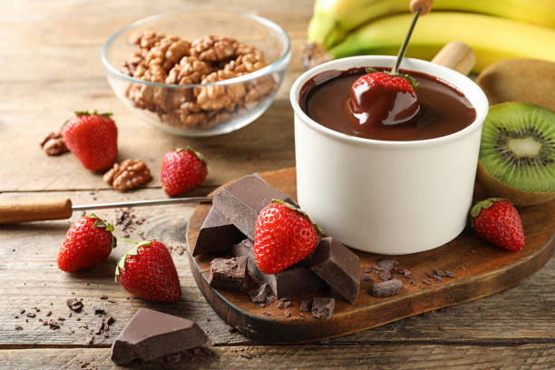 A delightful chocolate fondue setup with fresh strawberries, chocolate pieces, and a bowl of walnuts next to bananas.