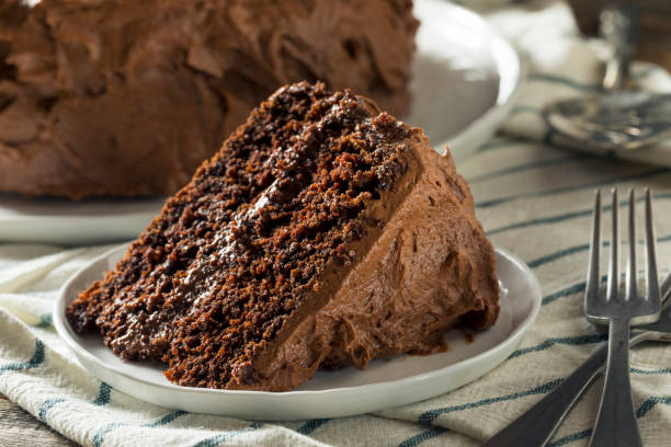 A slice of rich chocolate cake with creamy frosting on a white plate