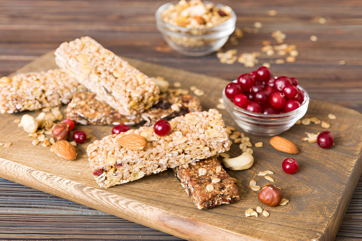 A wooden platter with assorted granola bars, nuts, and fresh cranberries.