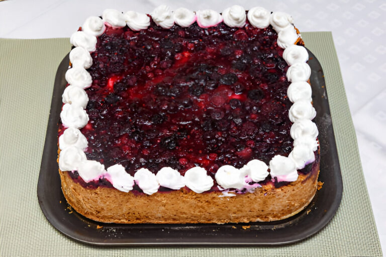 A square cake topped with a berry glaze and whipped cream, served on a black tray.