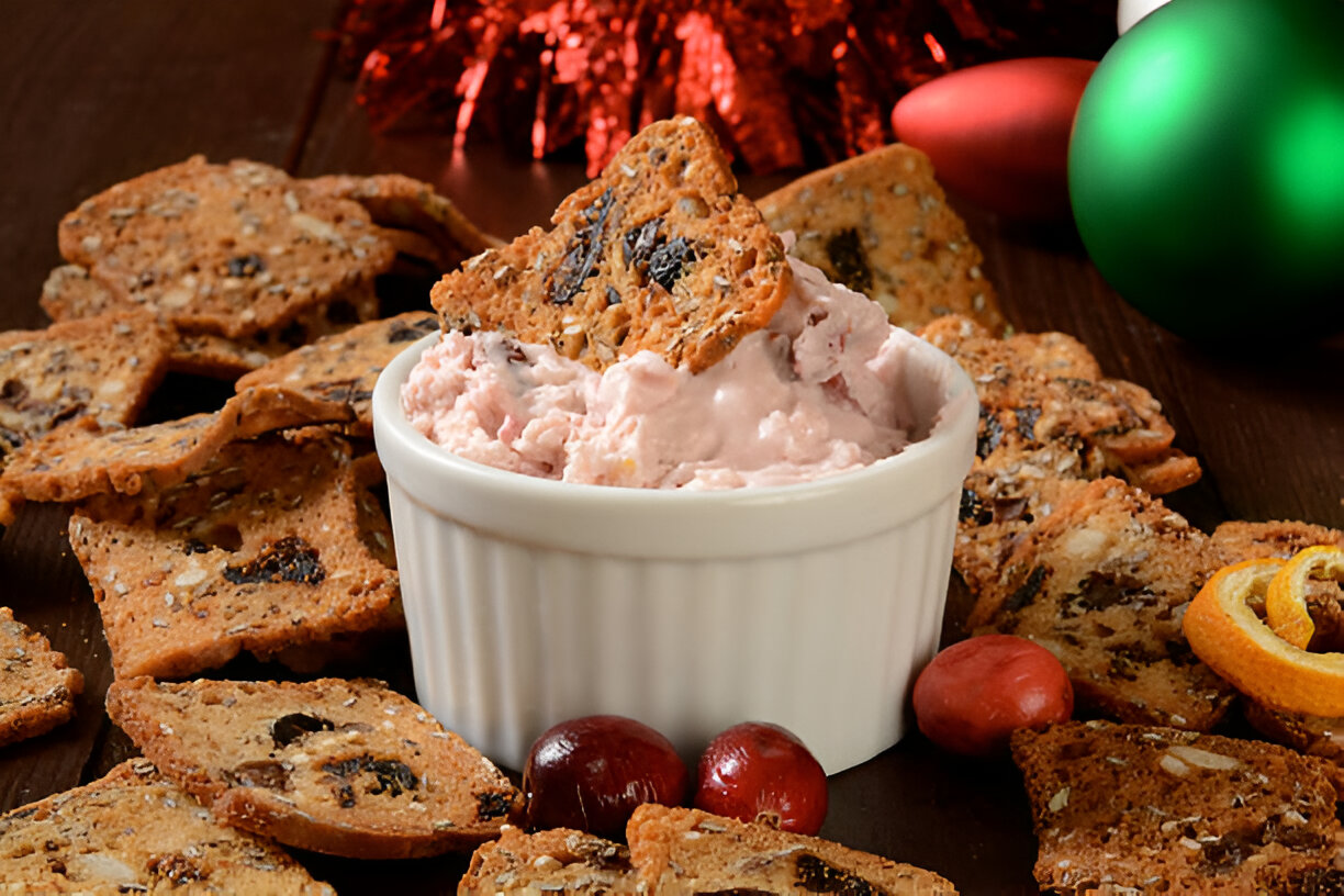 A bowl of pink cream cheese dip surrounded by crispy, thin crackers and festive decorations