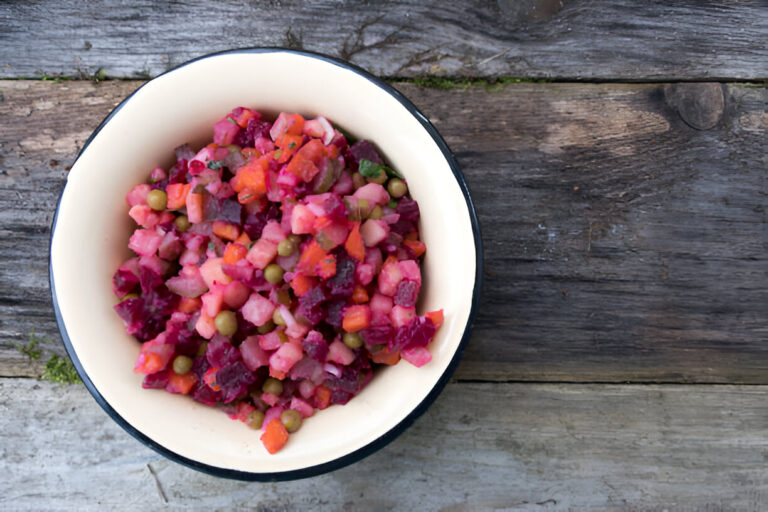 A colorful bowl of salad made with diced beets, carrots, and green peas against a rustic wooden background.