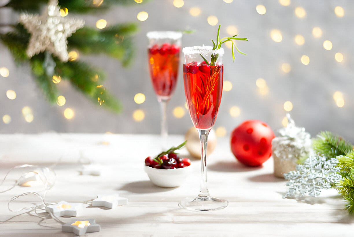 Two festive cocktails in champagne flutes surrounded by holiday decorations.