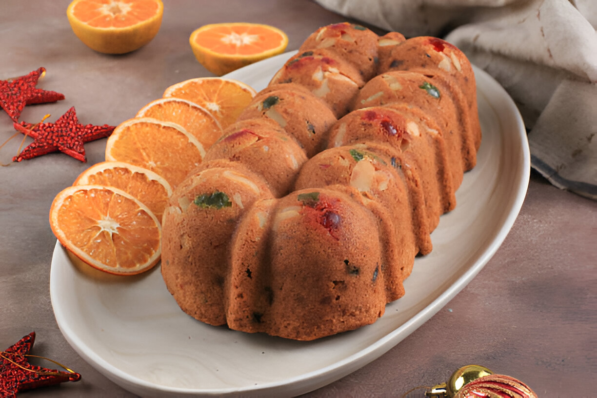 A festive Bundt cake garnished with colorful fruits, served with orange slices and decorative stars.