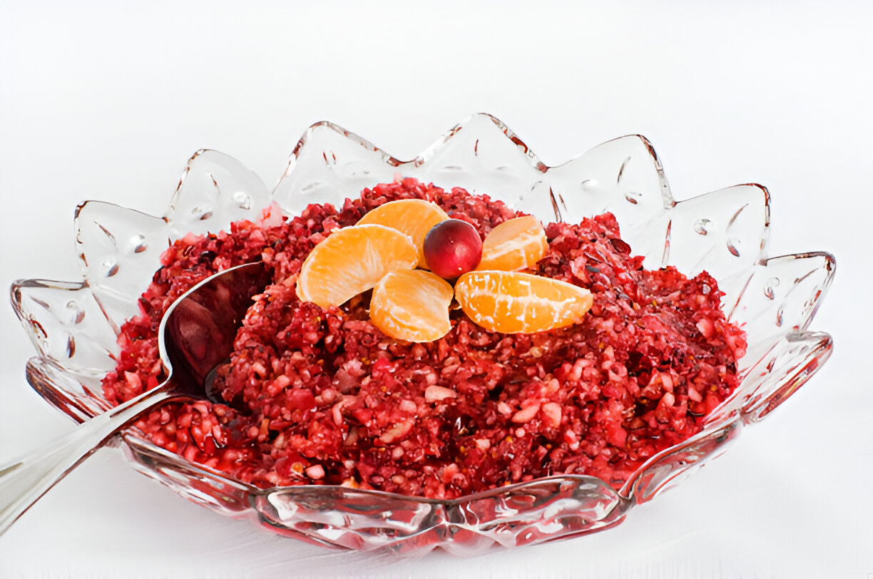 A colorful fruit salad served in a decorative glass bowl, featuring a blend of red and orange fruits.