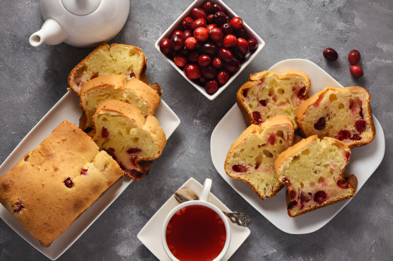 Sliced cranberry bread served with a cup of tea and fresh cranberries.