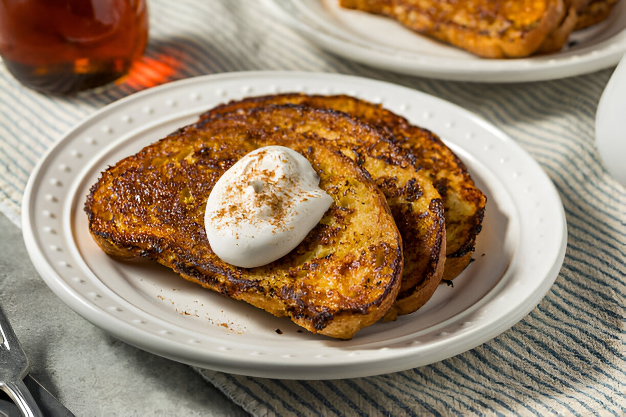 Three slices of golden-brown French toast topped with a dollop of whipped cream and sprinkled with cinnamon.