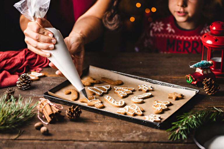 A person icing decorated gingerbread cookies on a baking tray with festive decorations in the background.