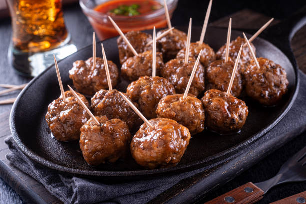 A platter of meatballs with toothpicks served on a cast iron skillet, accompanied by a small bowl of dipping sauce.