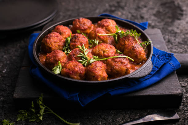 A serving of meatballs topped with fresh herbs in a cast iron skillet on a dark surface.