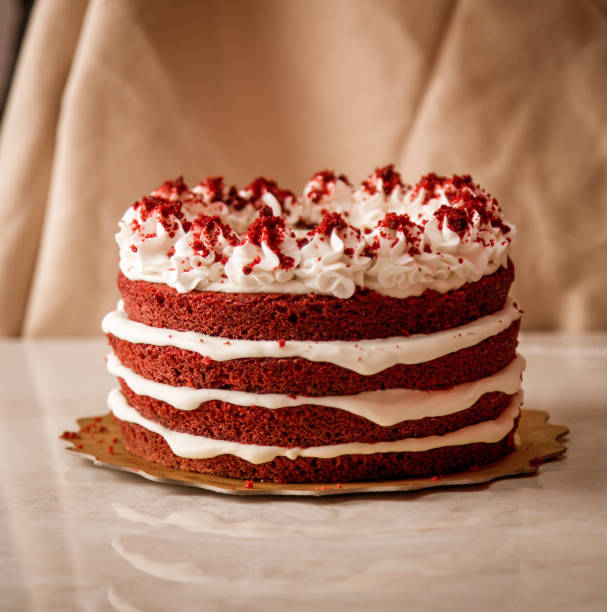 A delicious red velvet cake with three layers, topped with whipped cream and red crumbs, placed on a golden cake board.