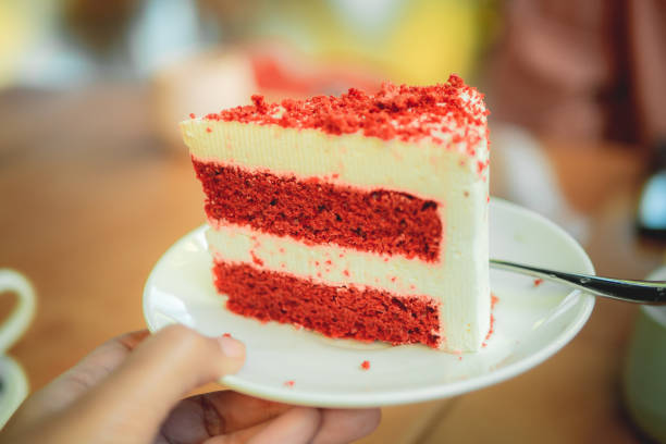 A slice of red velvet cake on a white plate held by a hand.