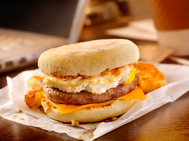 A delicious breakfast sandwich with egg, sausage, and cheddar cheese on an English muffin, served with a side of hash browns.