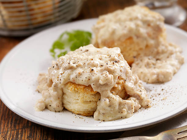 Close-up of two flaky biscuits topped with creamy sausage gravy and black pepper on a white plate.