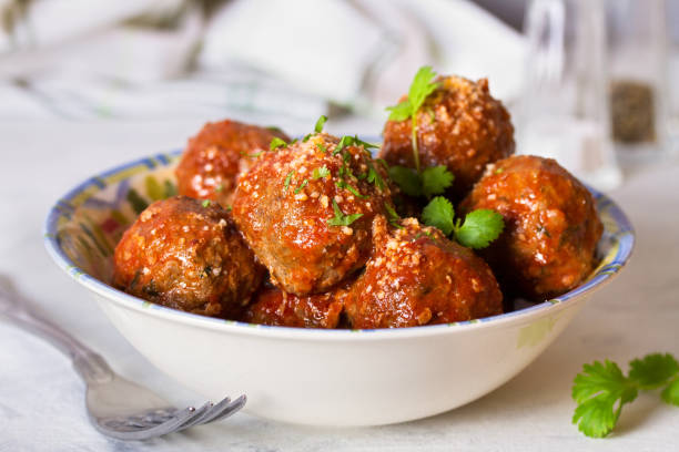 A bowl of savory meatballs covered in tomato sauce and garnished with herbs.