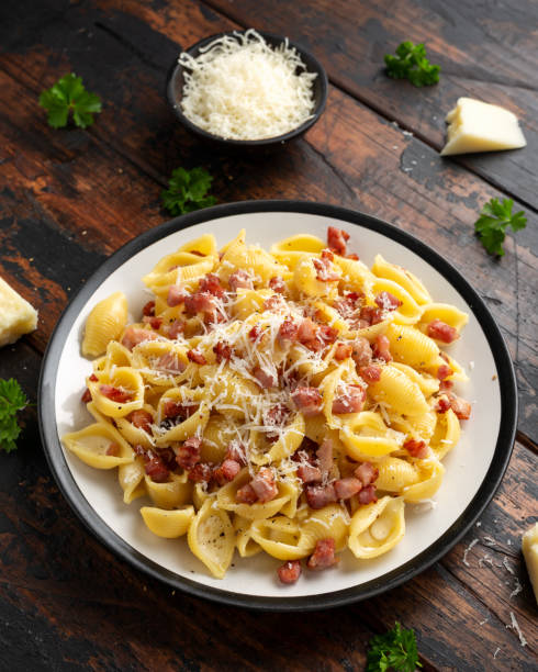 A plate of pasta with bacon bits and grated cheese on a wooden table