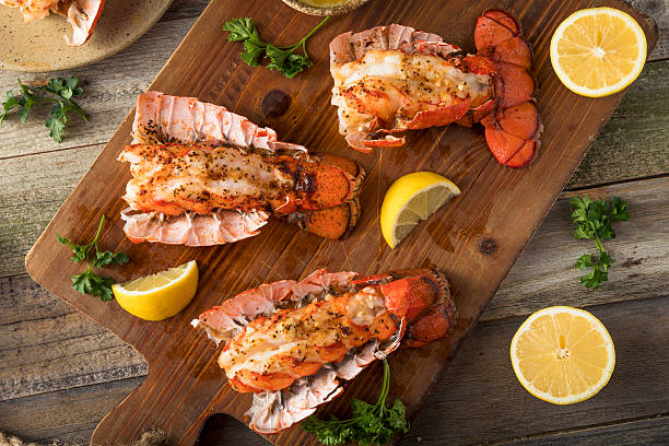 Grilled lobster tails served on a wooden cutting board with lemon wedges and parsley.