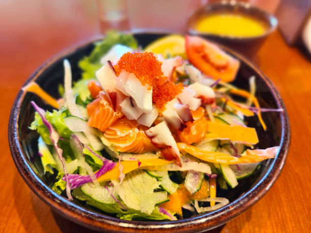 A vibrant salad with fresh vegetables, topped with salmon and orange roe, served in a dark bowl.