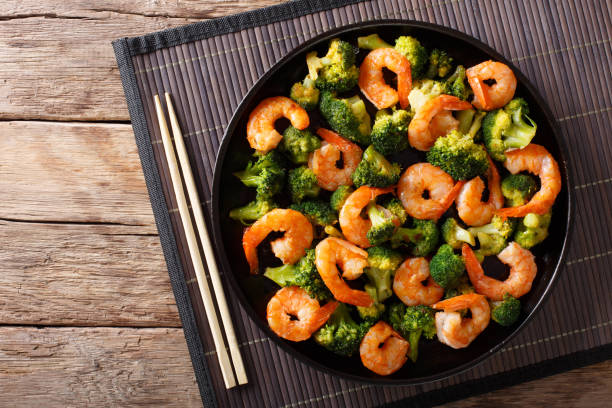 A black plate filled with shrimp and broccoli on a bamboo mat.