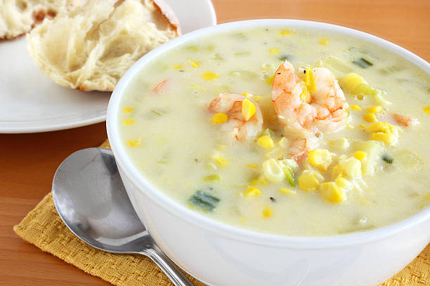 A bowl of shrimp and corn chowder served with bread on the side.