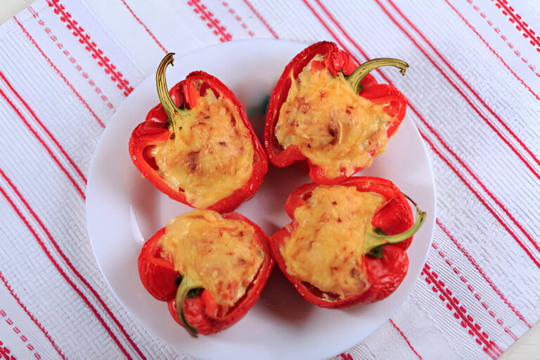 Four halved red bell peppers stuffed with a golden, cheesy filling on a white plate