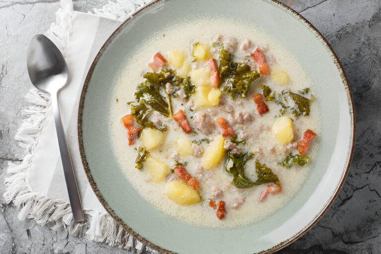 A bowl of creamy soup with sausage, kale, potatoes, and tomatoes on a decorative plate.