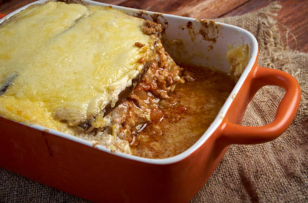 A serving of baked lasagna in an orange casserole dish, partially removed, with melted cheese on top and sauce around it.