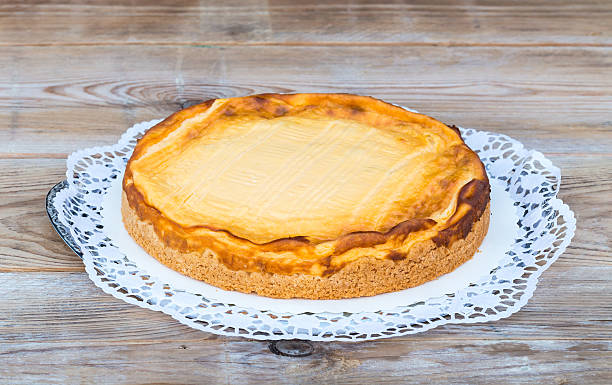 A round cheesecake on a lace doily atop a wooden surface.