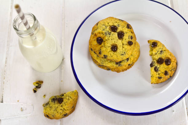 A plate of freshly baked chocolate chip cookies next to a bottle of milk with a straw.