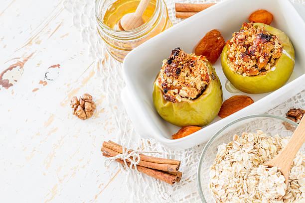 Baked green apples stuffed with oats and nuts, served on a white dish, with a jar of honey and cinnamon sticks nearby.