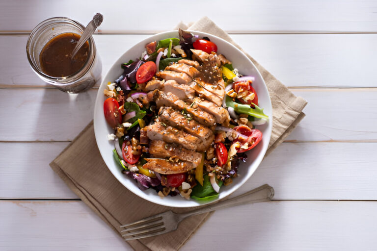 A healthy chicken salad served in a white bowl with a side of dressing