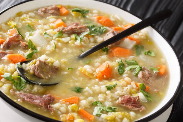 A bowl of hearty soup with chunks of beef, carrots, and leafy greens.