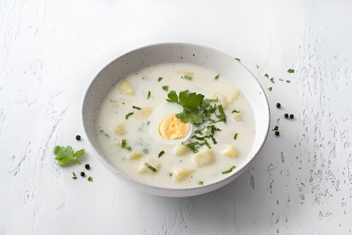 A bowl of creamy soup with boiled egg and fresh herbs.