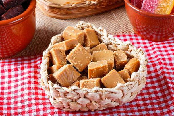 A heart-shaped wicker basket filled with pieces of caramel candy placed on a checkered tablecloth.